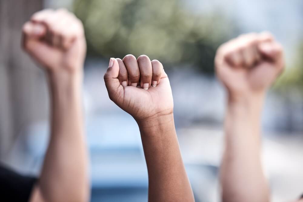 Three hands in the air with their fists closed showing they are ready to fight for human rights.