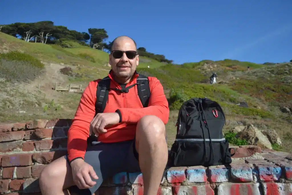 man sitting on mountain next to backpack