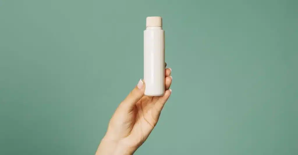 Hand holding a minimalist cream bottle, representing no product branding or packaging design.